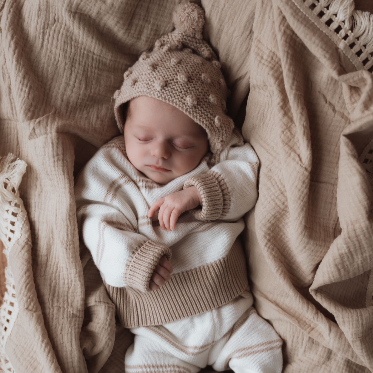 Een vrolijke baby met donker haar ligt op een witte deken met kanttextuur, draagt een knusse Yumi Baby-handdoekset voor 0-6 maanden en straalt met een brede, vrolijke glimlach.