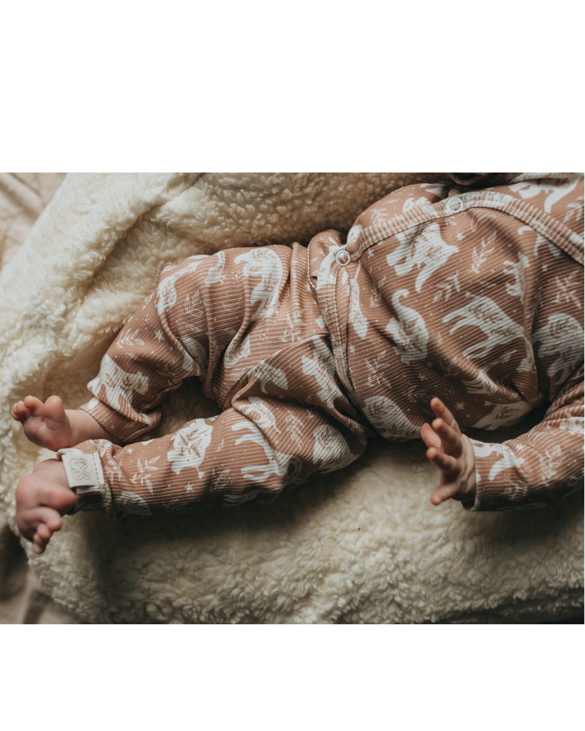 Een serene pasgeboren baby gekleed in een Yumi Baby Broekje Boho Jungle onesie gemaakt van OEKO-TEX gecertificeerd katoen en een bijpassend mutsje, vredig slapend in een knus rieten mandje gevoerd met een zachte, crèmekleurige deken.