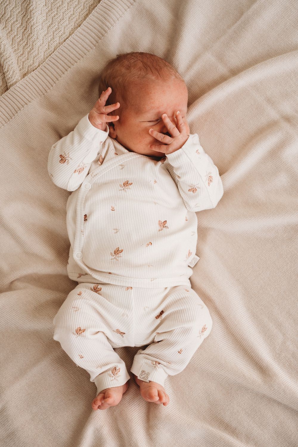 Vreedzame slaap: een pasgeboren baby rust rustig uit in een knusse outfit gemaakt van Yumi Baby's Overslagshirt Cocoa, die de pure onschuld van het vroege leven belichaamt.
