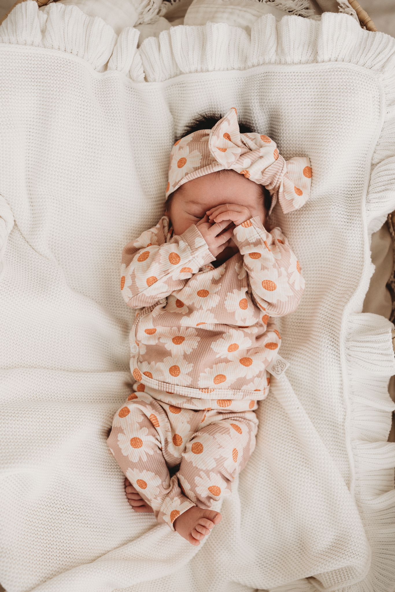Een vredige pasgeboren baby gehuld in een Overslagshirt Daisy Delight gemaakt van katoen OEKO TEX en bijpassende hoofdband, comfortabel genesteld in een knus wiegje, symbool voor de pure onschuld en sereniteit van Yumi Baby.
