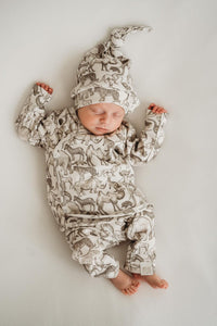 Een gezellige baby gekleed in een knus Yumi Baby Broekje Little Safari-outfit met een schattig bijpassend hoedje, ligt in een geweven mand, omringd door zachte, verkreukelde dekens, tevreden en vredig.