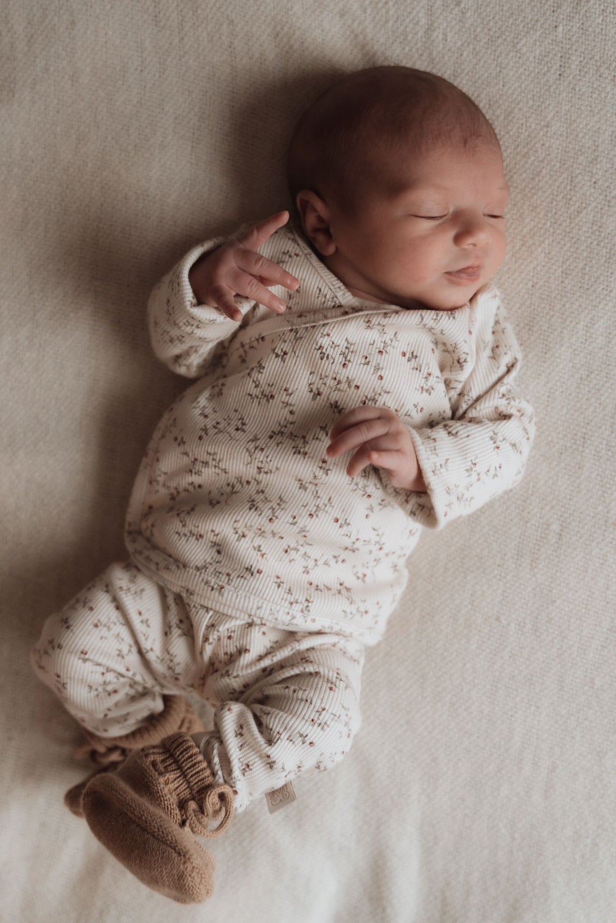 Vreedzame slaap: een pasgeboren baby slaapt stevig verpakt in warme tinten en gezellige texturen van OEKO-TEX gecertificeerde Osman Broekje Appeltakken, die onschuld en rust belichamen.