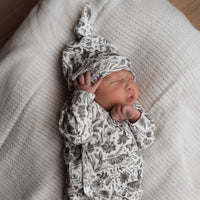 Een vredige pasgeboren baby gekleed in een Osman Overslagshirt Bunnies onesie en bijpassend mutsje, gemaakt van OEKO TEX katoen, slaapt heerlijk op een zacht, beige kussen.