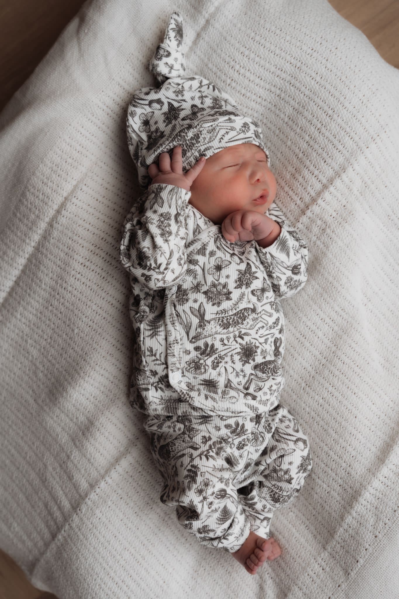 Een vredige pasgeboren baby gekleed in een Osman Overslagshirt Bunnies onesie en bijpassend mutsje, gemaakt van OEKO TEX katoen, slaapt heerlijk op een zacht, beige kussen.