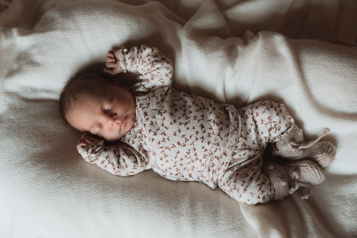 Vreedzame slaap van een pasgeboren baby gekleed in een knus Osman Overslagshirt Brown Leafs onesie, compleet met een bijpassende hoed en slofjes, allemaal gecertificeerd door OEKO TEX.