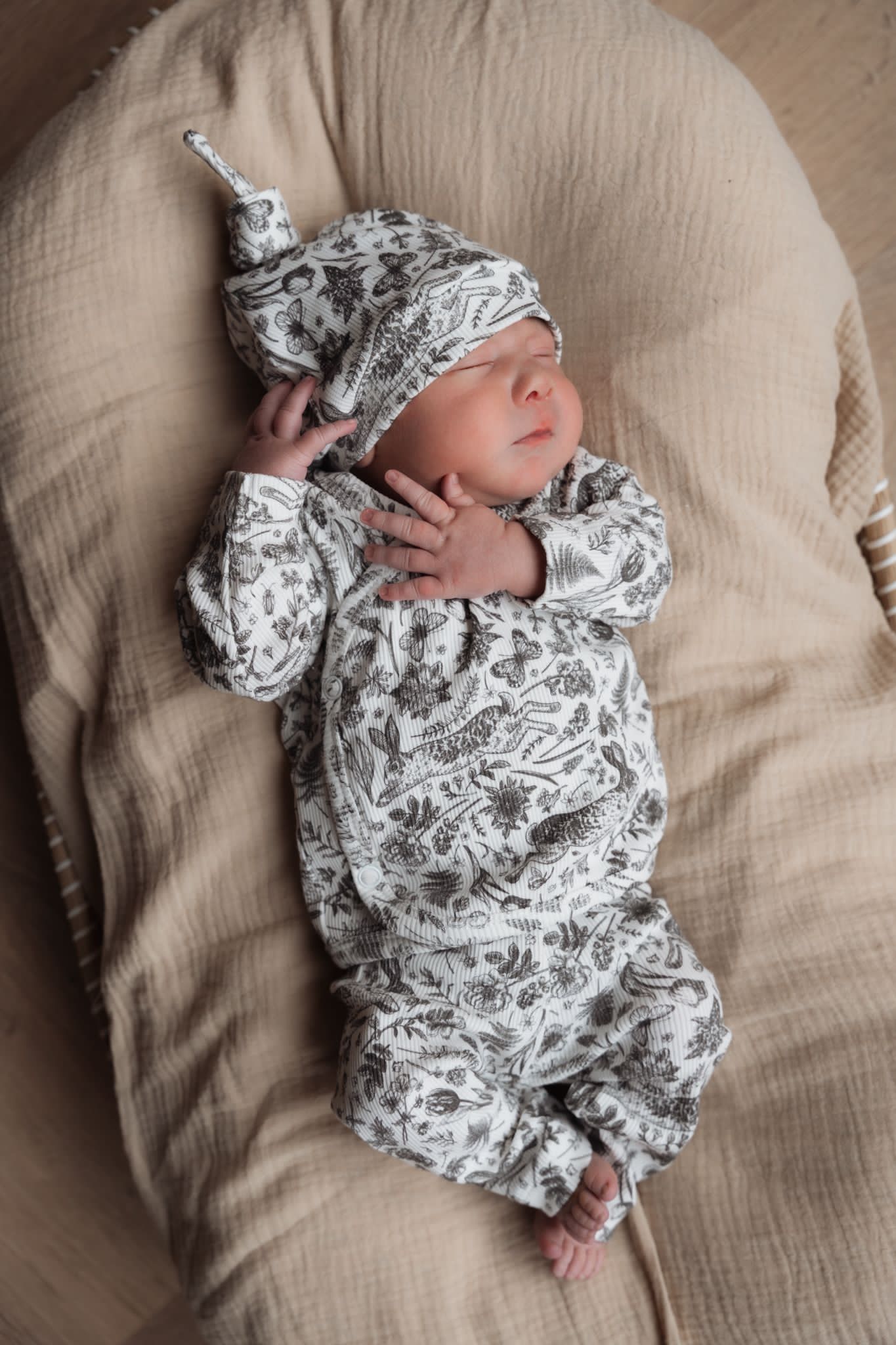 Een vredige pasgeborene slaapt lekker in een Yumi Baby Overslagshirt Bunnies onesie en bijpassend mutsje, gewiegd in een gezellig stoffen nestje.