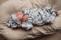 Een stille pasgeboren baby, gehuld in een babyoutfit met patronen en een Muts Bunnies van het merk Osman, slaapt zacht op een zachte, witte deken.