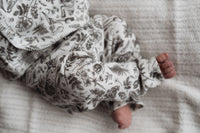 Een vredige pasgeboren baby in een rompertje met patroon en Yumi Baby's Broekje Konijntjes, heerlijk slapend op een zachte, gestructureerde deken.
