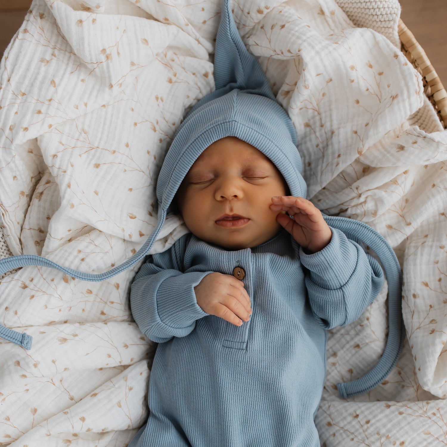 Een pasgeboren baby slaapt rustig, ingewikkeld in een knusse blauwe outfit met een Yumi Baby Strikmutsje Blue Sky, die de sereniteit.
