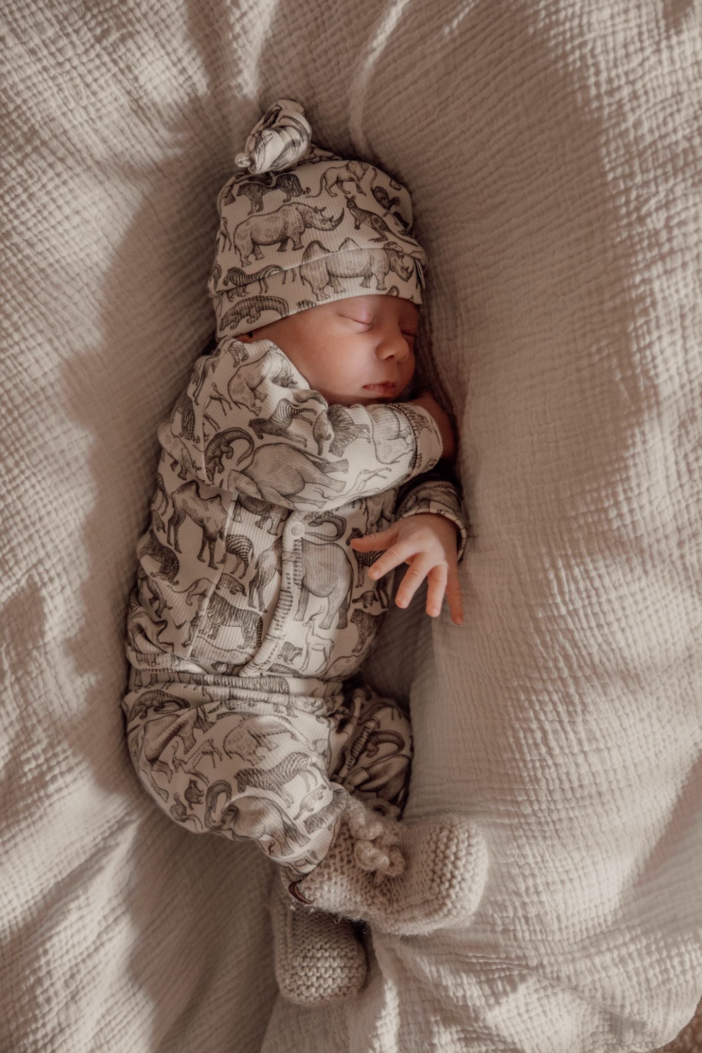 Een vredige pasgeborene, gezellig ingebakerd in een Zijdezacht Little Safari dekentje en outfitje, zuigt tevreden aan een speentje.
