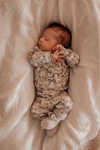 Een vredige pasgeborene, gezellig ingebakerd in een Zijdezacht Little Safari dekentje en outfitje, zuigt tevreden aan een speentje.