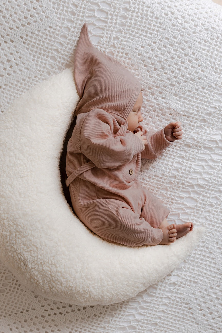 Een stille pasgeboren baby, gekleed in een gezellige bruine onesie met een puntige capuchon en een Yumi Baby Strikmutsje Blush, comfortabel.