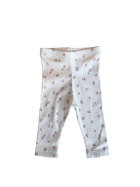 Een vredige pasgeboren baby die slaapt, gekleed in een schattig bedrukt Yumi Baby Broekje Peach Blossom onesie en bijpassend hoedje, liggend op een zacht wit oppervlak met de armen zachtjes omhoog bij het gezicht.