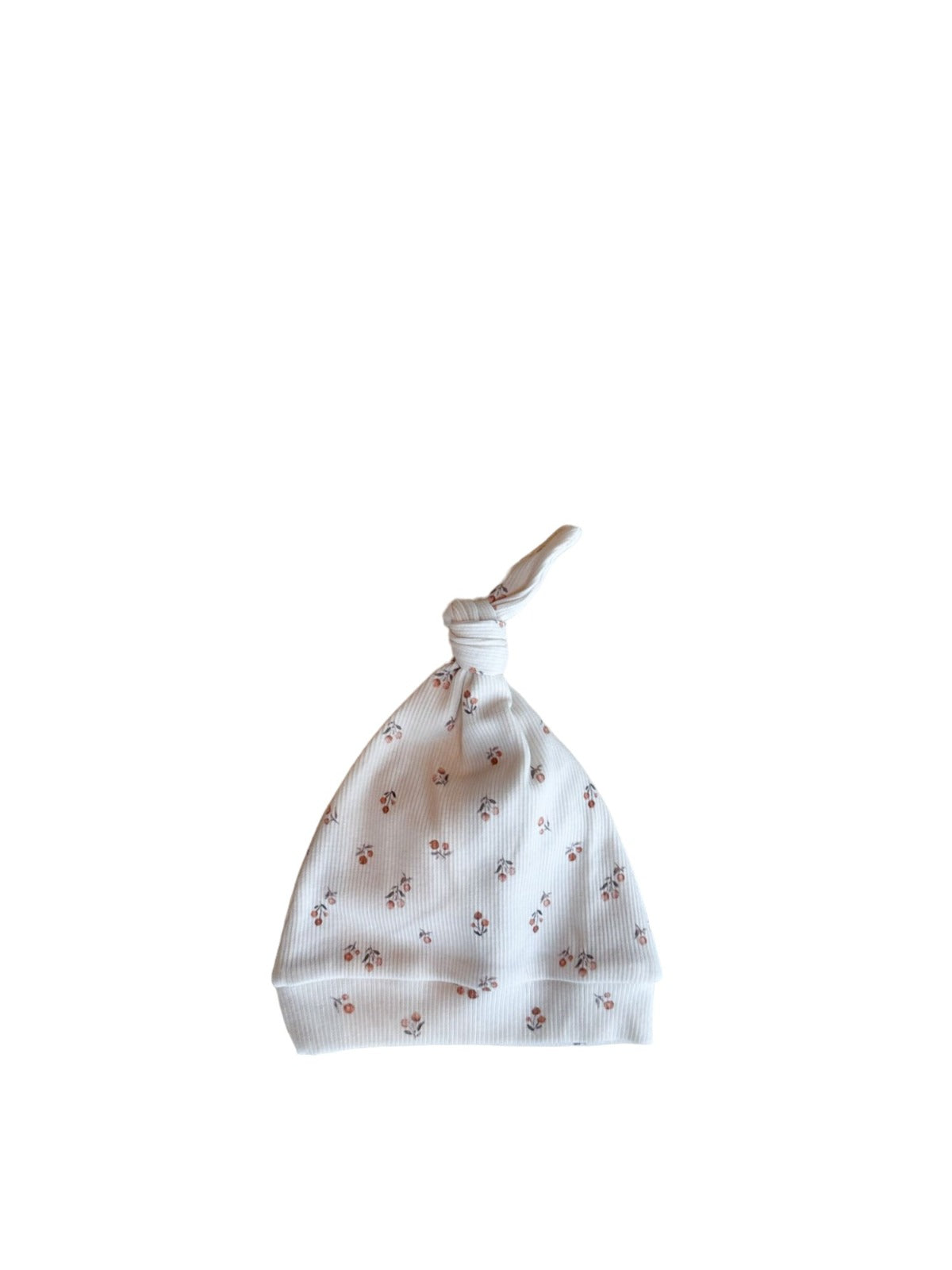 Een vredige pasgeboren baby in een schattig wit outfitje met printjes, wegdommelend met kleine handjes bij het gezichtje, lekker weggestopt op een zacht, zijdezacht dekentje met een Yumi Baby Muts Peach Blossom op het hoofdje.