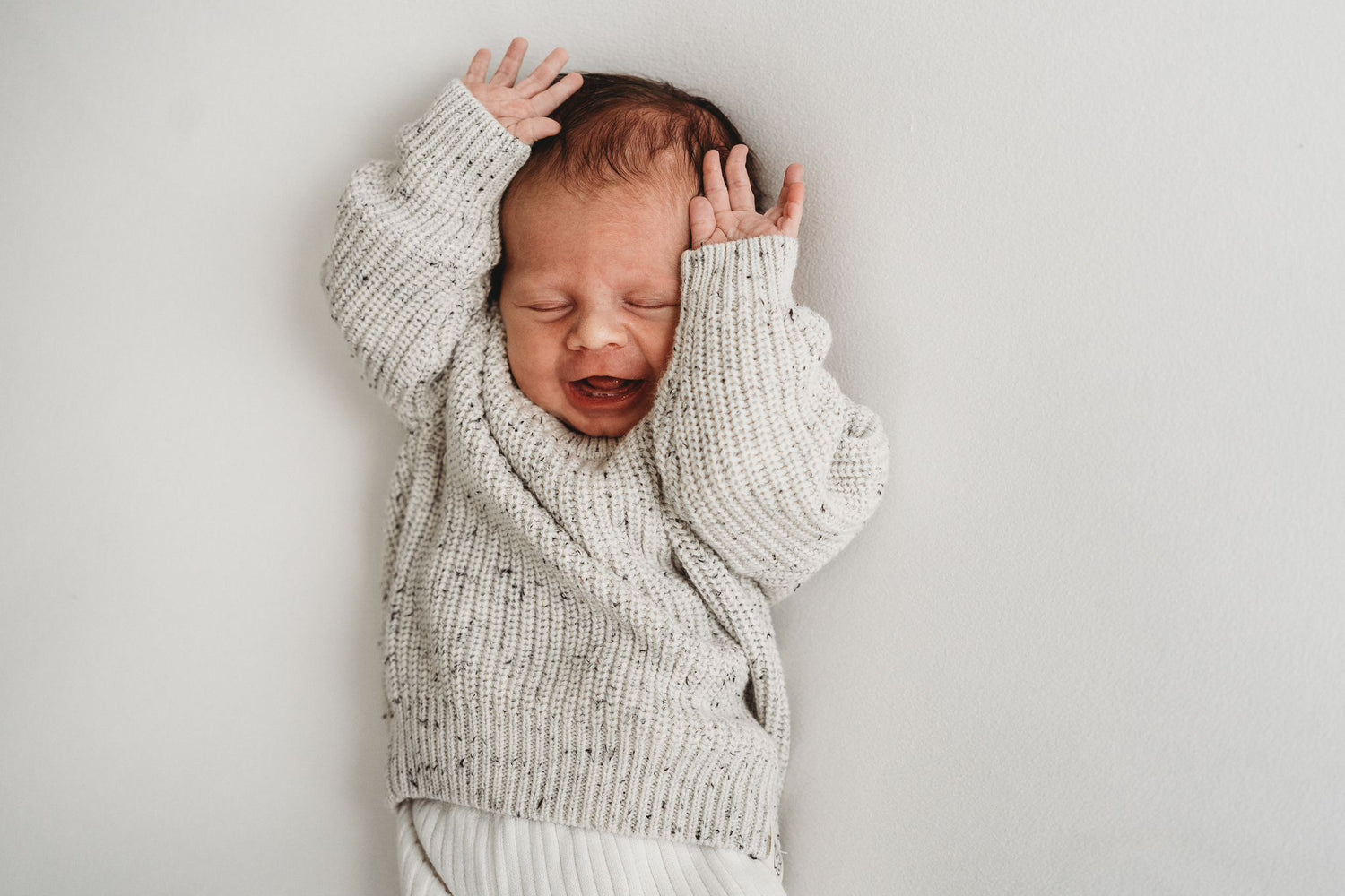 Rust voor pasgeborenen: baby gewikkeld in een knusse Yumi Baby Knitted trui Salt & Pepper, rustig slapend in een 100% katoenen gebreide set.