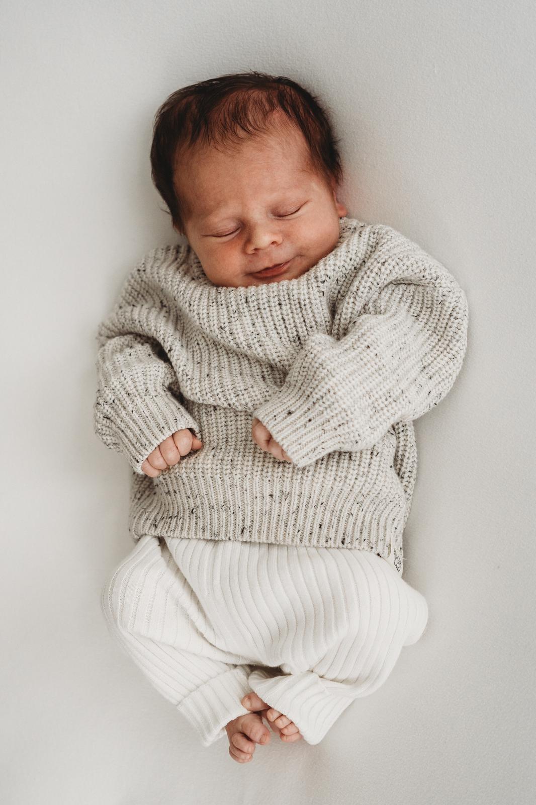 Rust voor pasgeborenen: baby gewikkeld in een knusse Yumi Baby Knitted trui Salt & Pepper, rustig slapend in een 100% katoenen gebreide set.