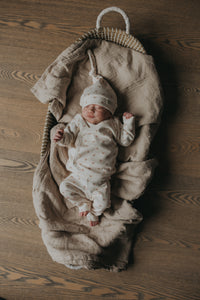 Een serene pasgeborene slaapt vredig in een knus mandje, lekker naast een zachte teddybeer, gekleed in een Yumi Baby Overslagshirt Tiny Tulip, symbool voor onschuld en een nieuw begin.