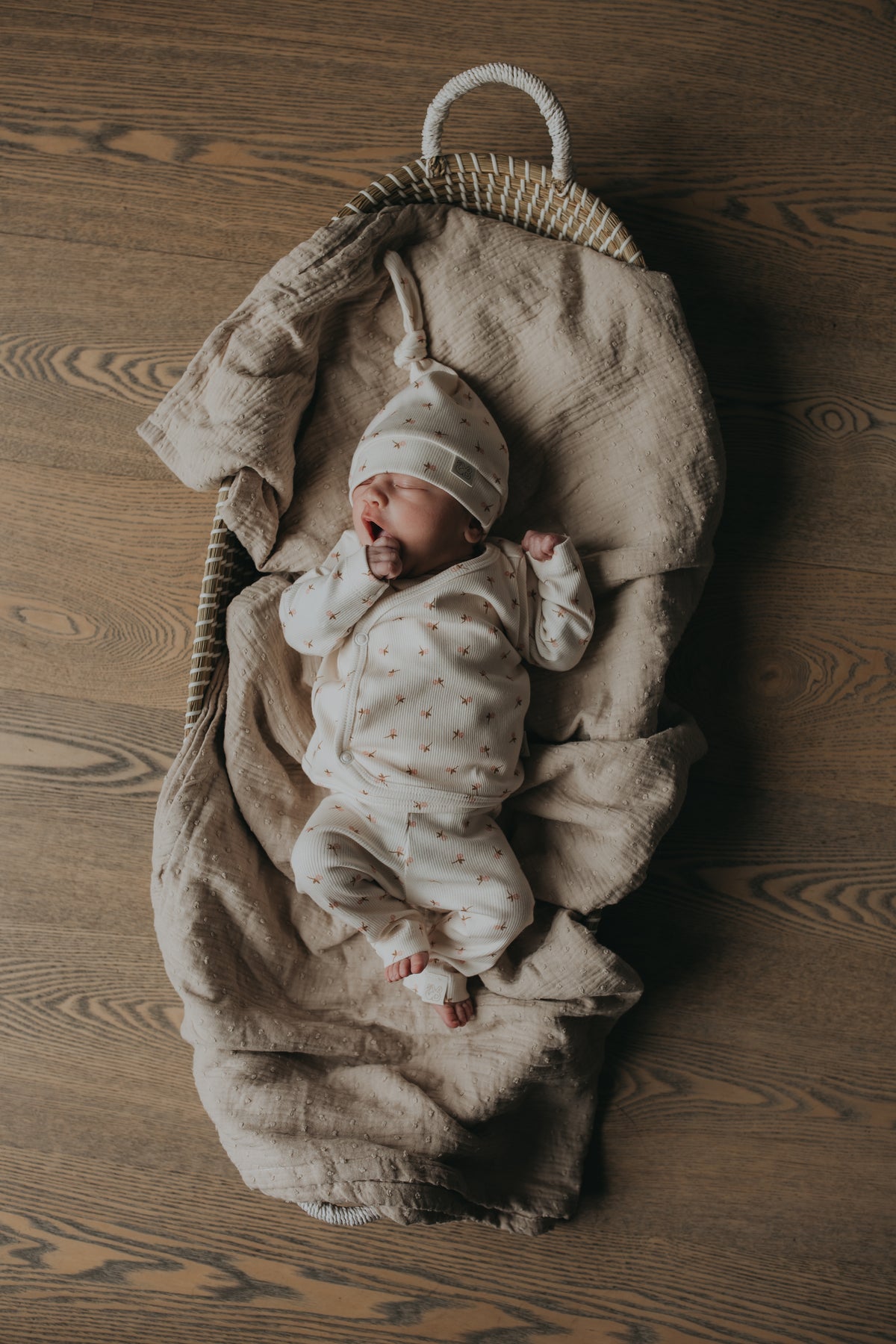 Een serene pasgeborene slaapt vredig in een knus mandje, lekker naast een zachte teddybeer, gekleed in een Yumi Baby Overslagshirt Tiny Tulip, symbool voor onschuld en een nieuw begin.