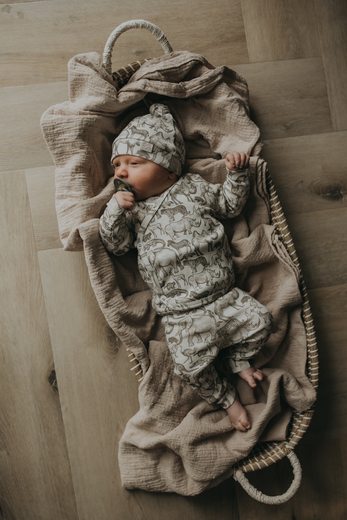Een vredige pasgeborene, gezellig ingebakerd in een Zijdezacht Little Safari dekentje en outfitje, zuigt tevreden aan een speentje.