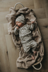 Een vredige pasgeborene, gezellig ingebakerd in een Zijdezacht Little Safari dekentje en outfitje, zuigt tevreden aan een speentje.