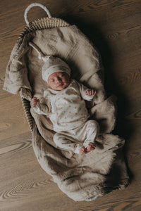 Een serene pasgeborene slaapt vredig in een knus mandje, lekker naast een zachte teddybeer, gekleed in een Yumi Baby Overslagshirt Tiny Tulip, symbool voor onschuld en een nieuw begin.