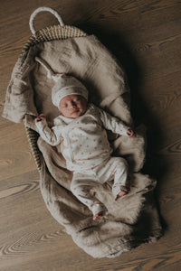 Een serene pasgeborene slaapt vredig in een knus mandje, lekker naast een zachte teddybeer, gekleed in een Yumi Baby Overslagshirt Tiny Tulip, symbool voor onschuld en een nieuw begin.