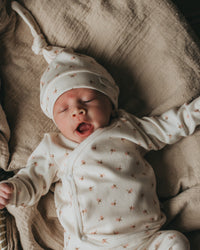 Een serene pasgeborene slaapt vredig in een knus mandje, lekker naast een zachte teddybeer, gekleed in een Yumi Baby Overslagshirt Tiny Tulip, symbool voor onschuld en een nieuw begin.