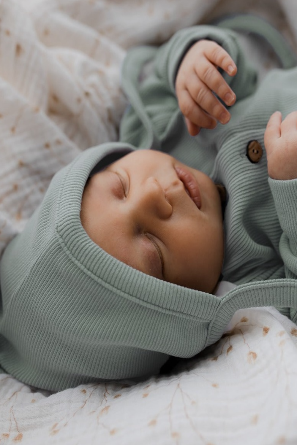 Een vredig kindje slaapt heerlijk, gekleed in een knus groen Yumi Baby Boxpakje Jade Treasure van hoogwaardig katoen, met bijpassend mutsje, comfortabel gelegen op een zachte deken met patroon.