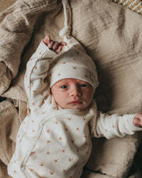 Een gapende baby gekleed in een knus rompertje met een bijpassend pasgeboren Muts Tiny Tulip babymutsje van Yumi Baby, comfortabel genesteld in een geweven mand op een zachte, zijdezachte deken.
