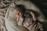Een vredige pasgeboren baby slaapt knus in een geweven mand, gezellig gekleed in een Yumi Baby Boho Jungle overslagshirt en bijpassend mutsje, met zachte OEKO-TEX gecertificeerde katoenen dekens voor extra comfort.