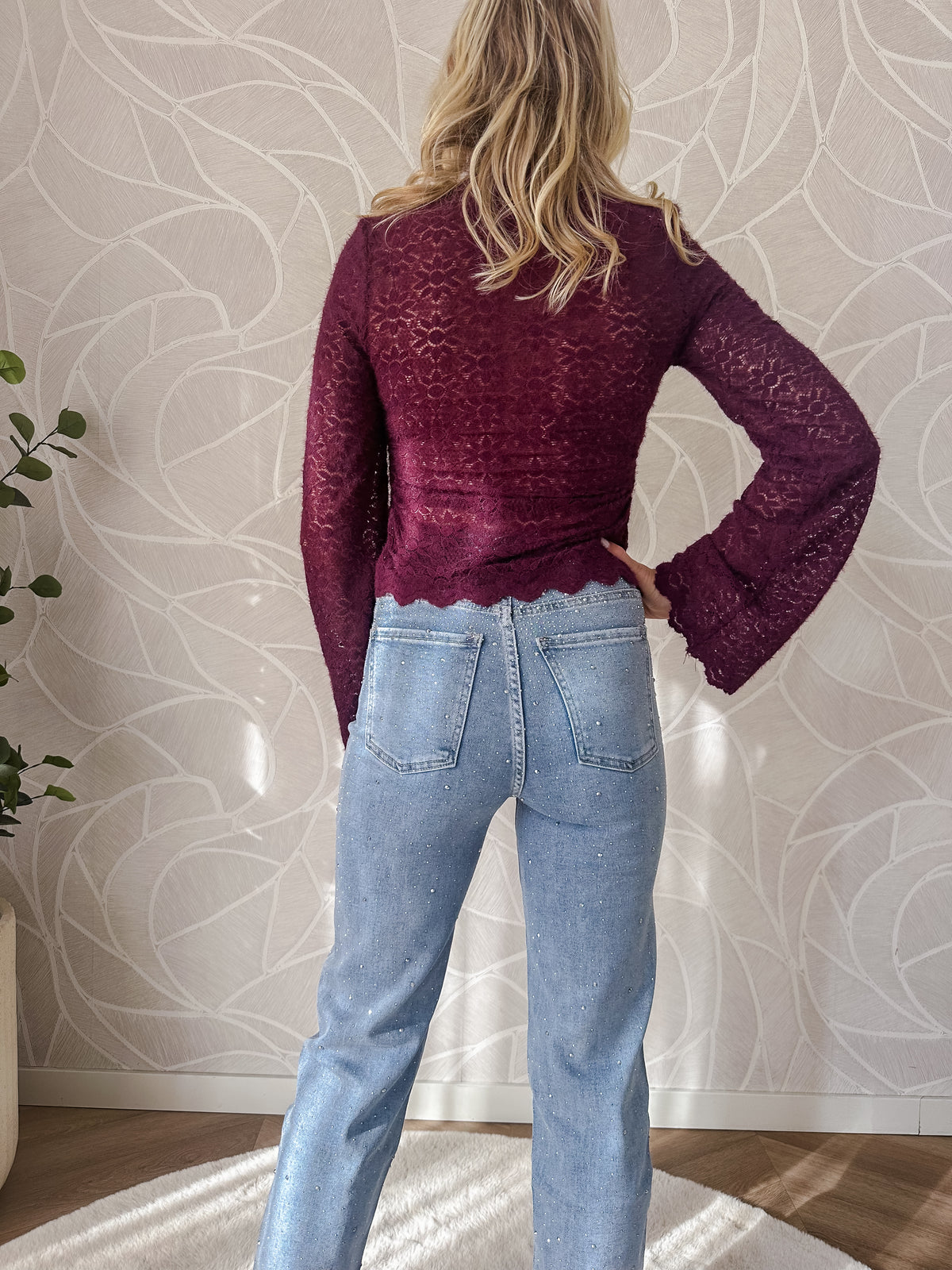 Model toont achterkant broek stretch jeans licht blauw met diamantjes en burgundy top