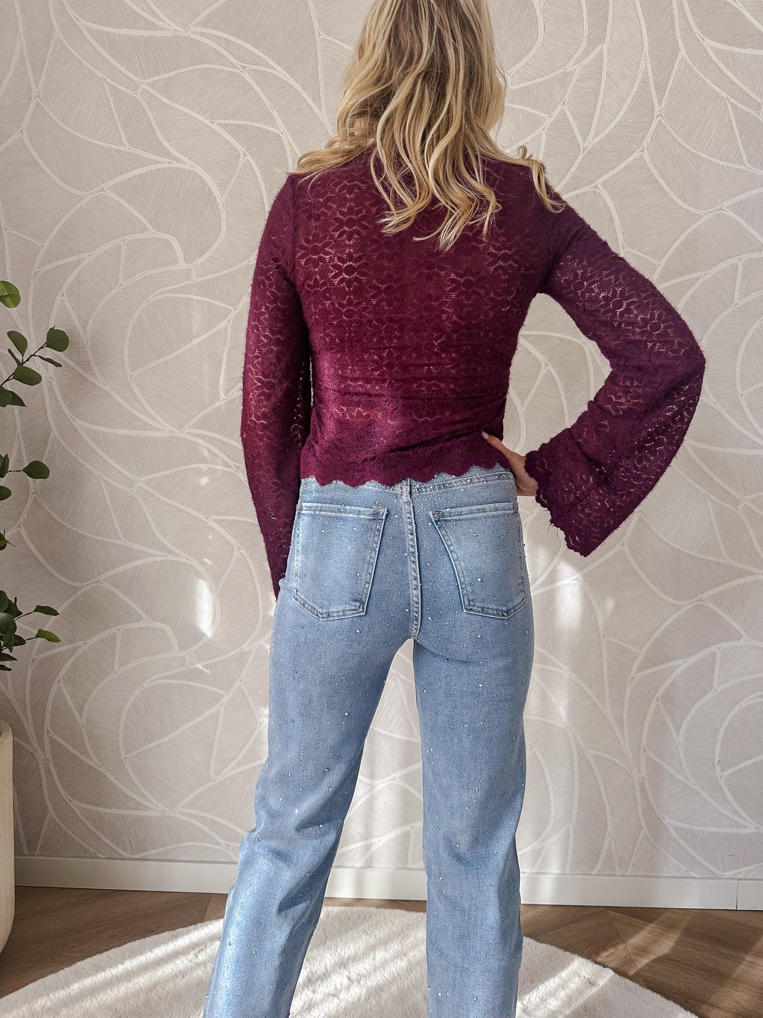 Model toont achterkant broek stretch jeans licht blauw met diamantjes en burgundy top