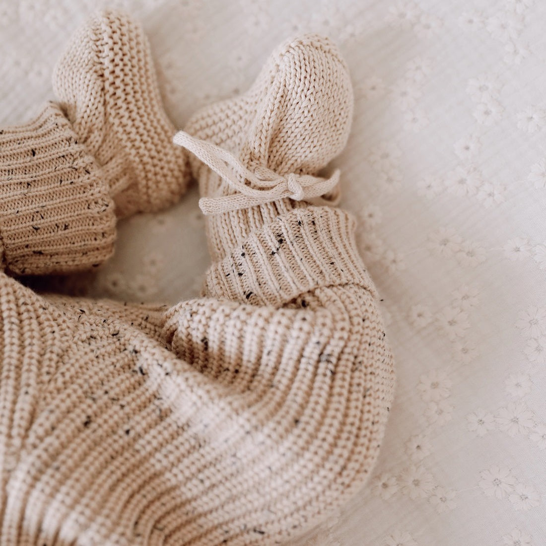 Een vredige baby slaapt heerlijk in een knus beige Yumi Baby Gebreide Set-outfit, met een zachte hoofdband en een klein knuffelkonijntje aan haar zijde.