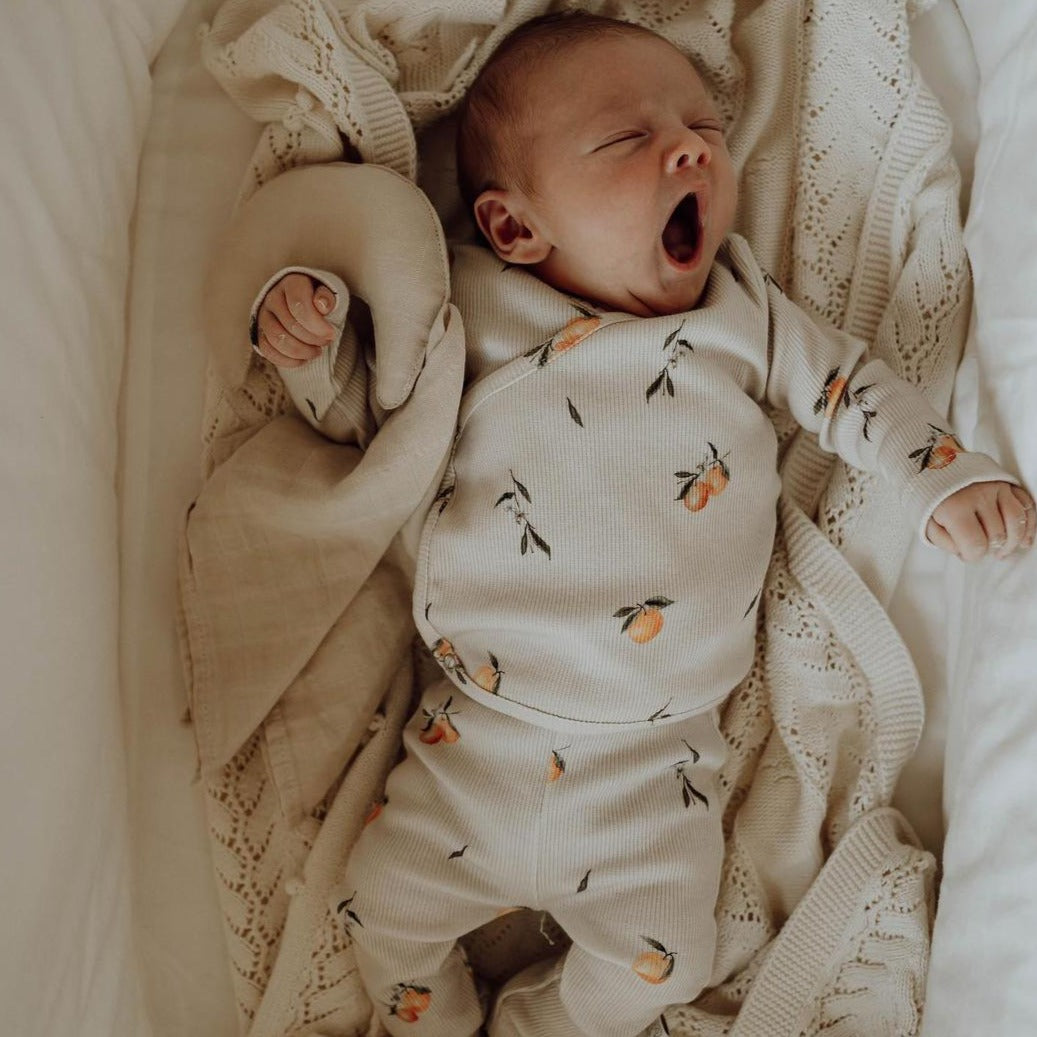 Een vredige pasgeboren baby slaapt heerlijk, lekker weggestopt in een zachte, OEKO-TEX gecertificeerde Yumi Babydeken met een geruststellend halvemaanvormig kussen dat hem omarmt.