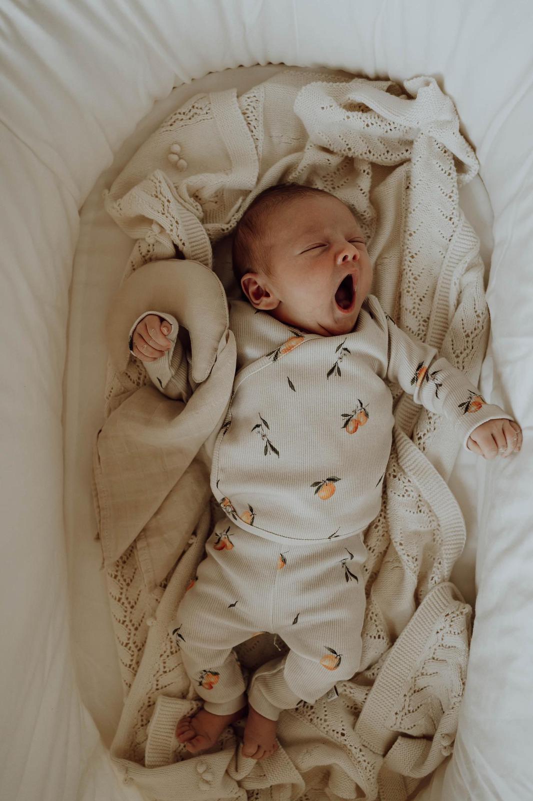 Een vredige pasgeboren baby slaapt heerlijk, ingebakerd in een Osman Overslagshirt Oranjebeige met een zacht patroon, dat rust en onschuld uitstraalt. De inbakerdoek is gemaakt van OEKO-TEX katoen.
