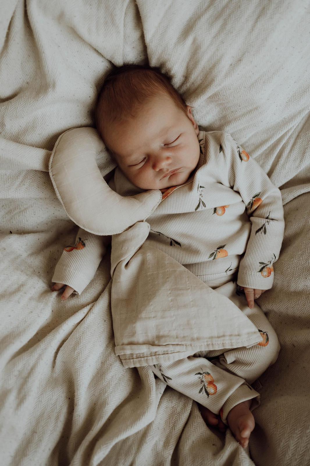 Een vredige pasgeboren baby slaapt heerlijk, ingebakerd in een Osman Overslagshirt Oranjebeige met een zacht patroon, dat rust en onschuld uitstraalt. De inbakerdoek is gemaakt van OEKO-TEX katoen.