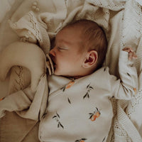 Een vredig slapende pasgeboren baby, gebundeld in een Yumi Baby overslagshirt Oranges Beige van OEKO TEX katoen, liggend op een gebreide deken.