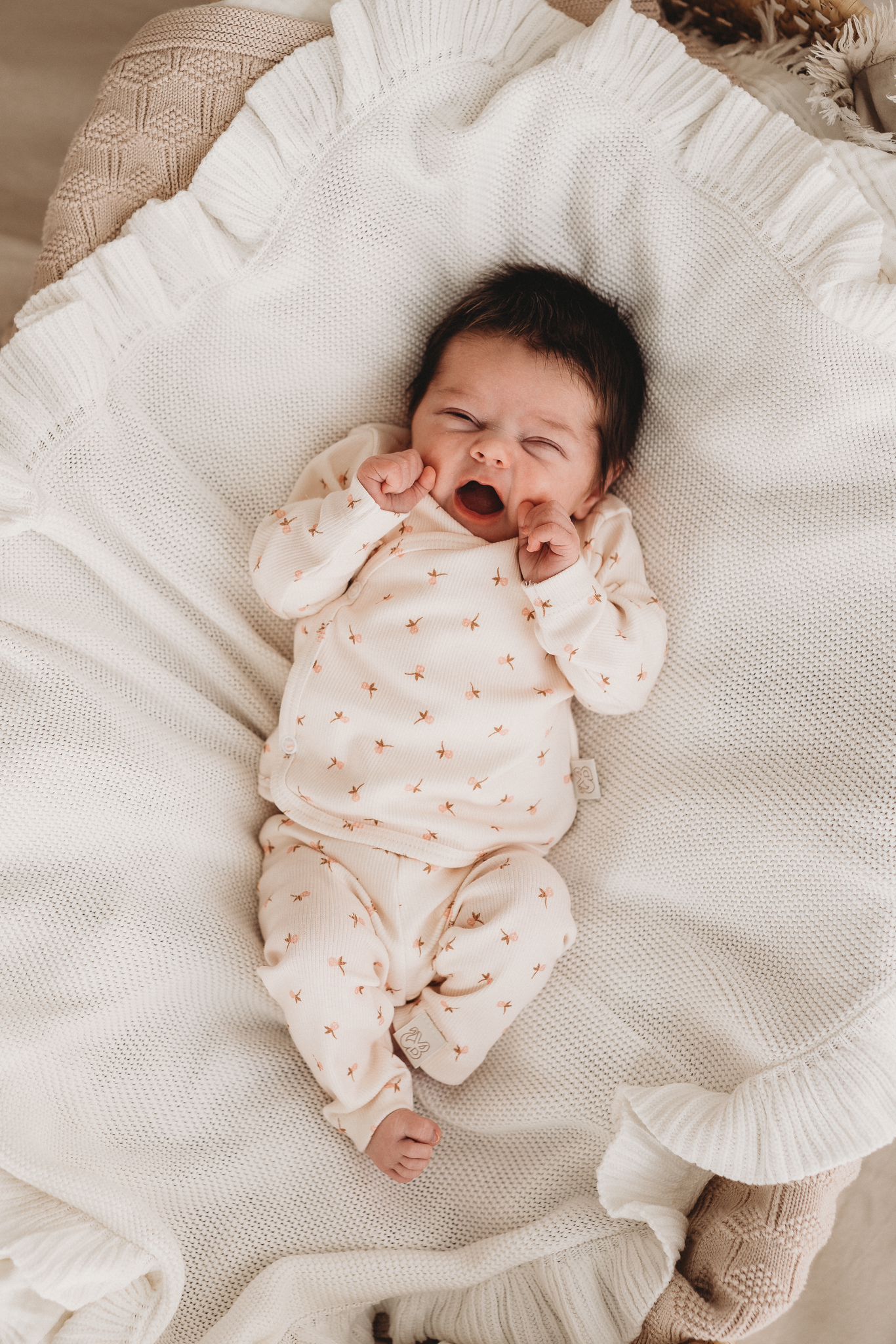 Een serene pasgeborene slaapt vredig in een knus mandje, lekker naast een zachte teddybeer, gekleed in een Yumi Baby Overslagshirt Tiny Tulip, symbool voor onschuld en een nieuw begin.