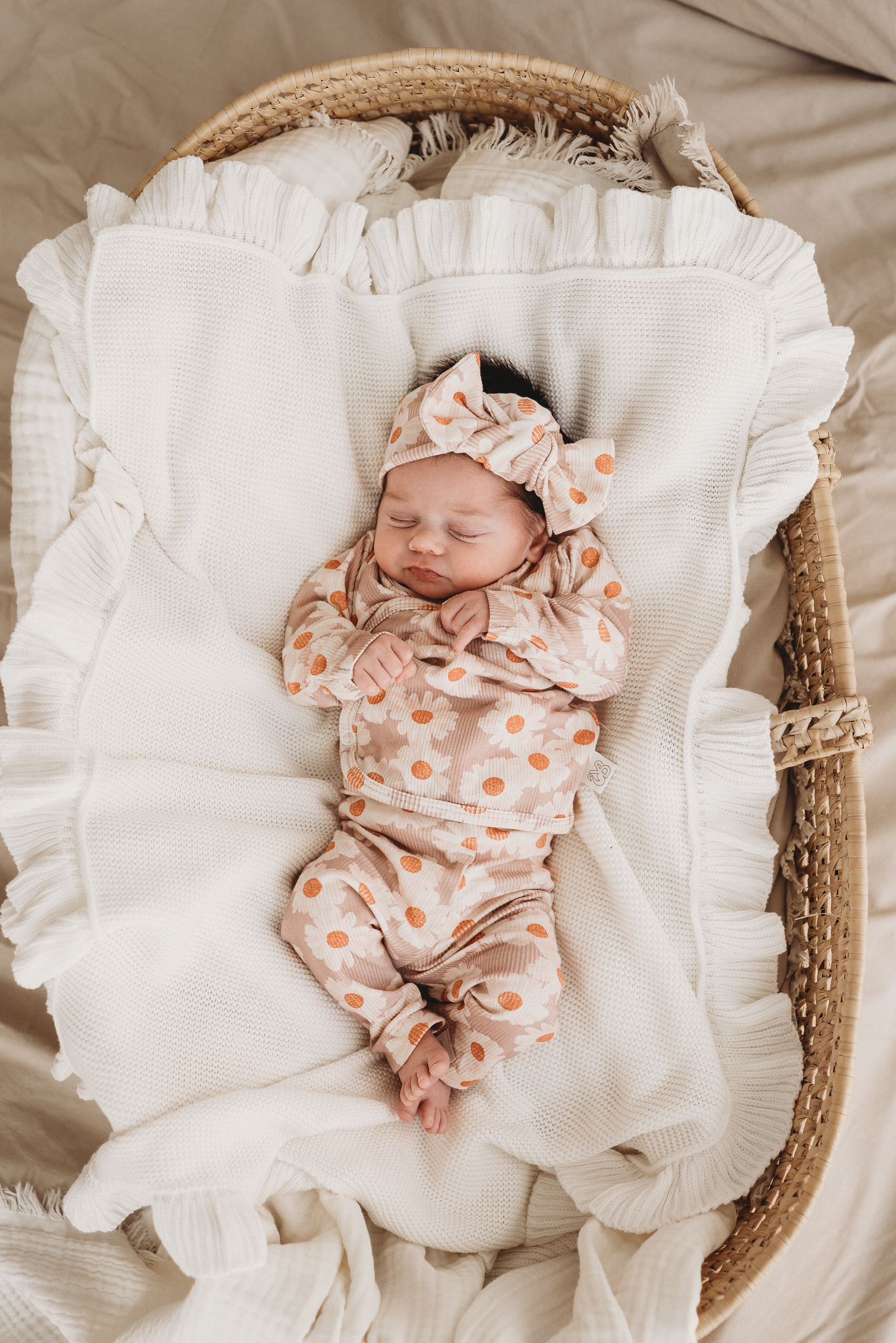 Een vredige pasgeboren baby gekleed in een Yumi Baby Haarband Daisy Delight slaapt heerlijk in een gezellig geweven mandje.