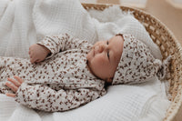 Een vredige pasgeboren baby, gekleed in een schattig Boxpakje Brown Leafs van hoogwaardig katoen en bijpassend mutsje, wegdommelend terwijl hij comfortabel tussen de zachte kussens op een knus bed ligt. Merk: Yumibaby.