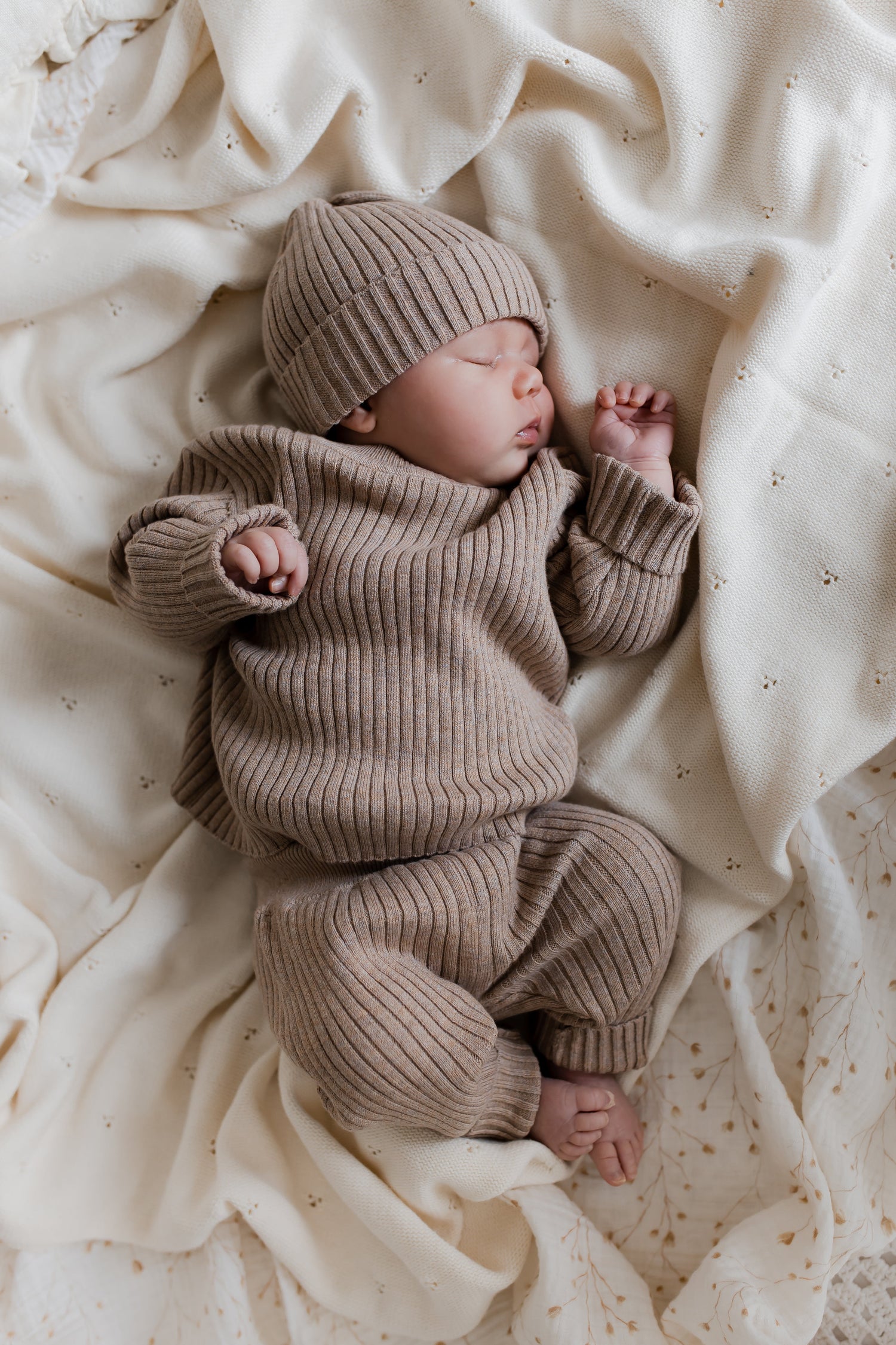 Een vredige baby slaapt heerlijk, gehuld in een Yumi Baby gebreide trui cacao schatje, liggend op een zacht beige dekentje.