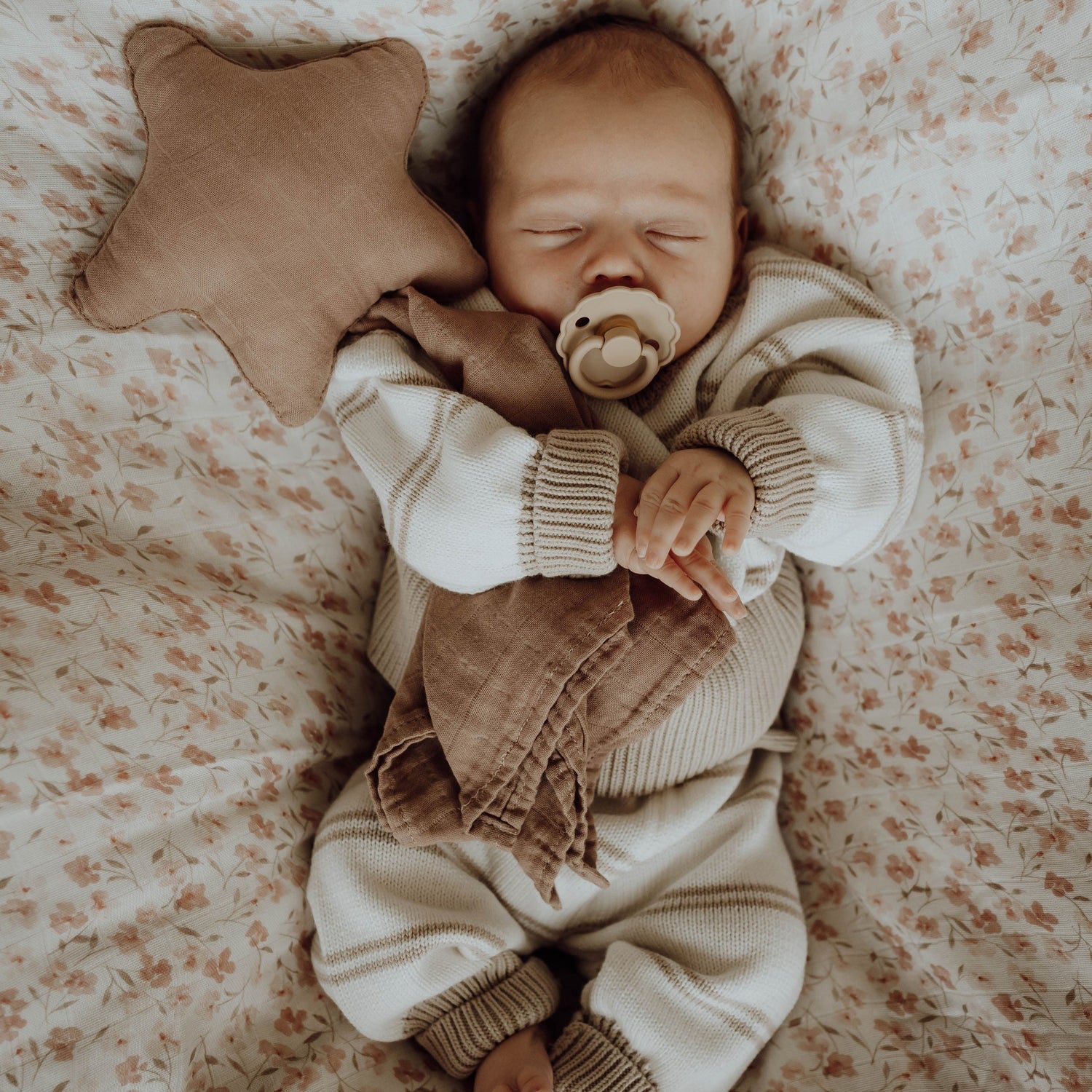 Vreedzaam slapen: een tevreden baby dut met een speentje, lekker in een knusse trui en lekker geknuffeld door een Yumi Baby Knuffeldoekje Starlight.