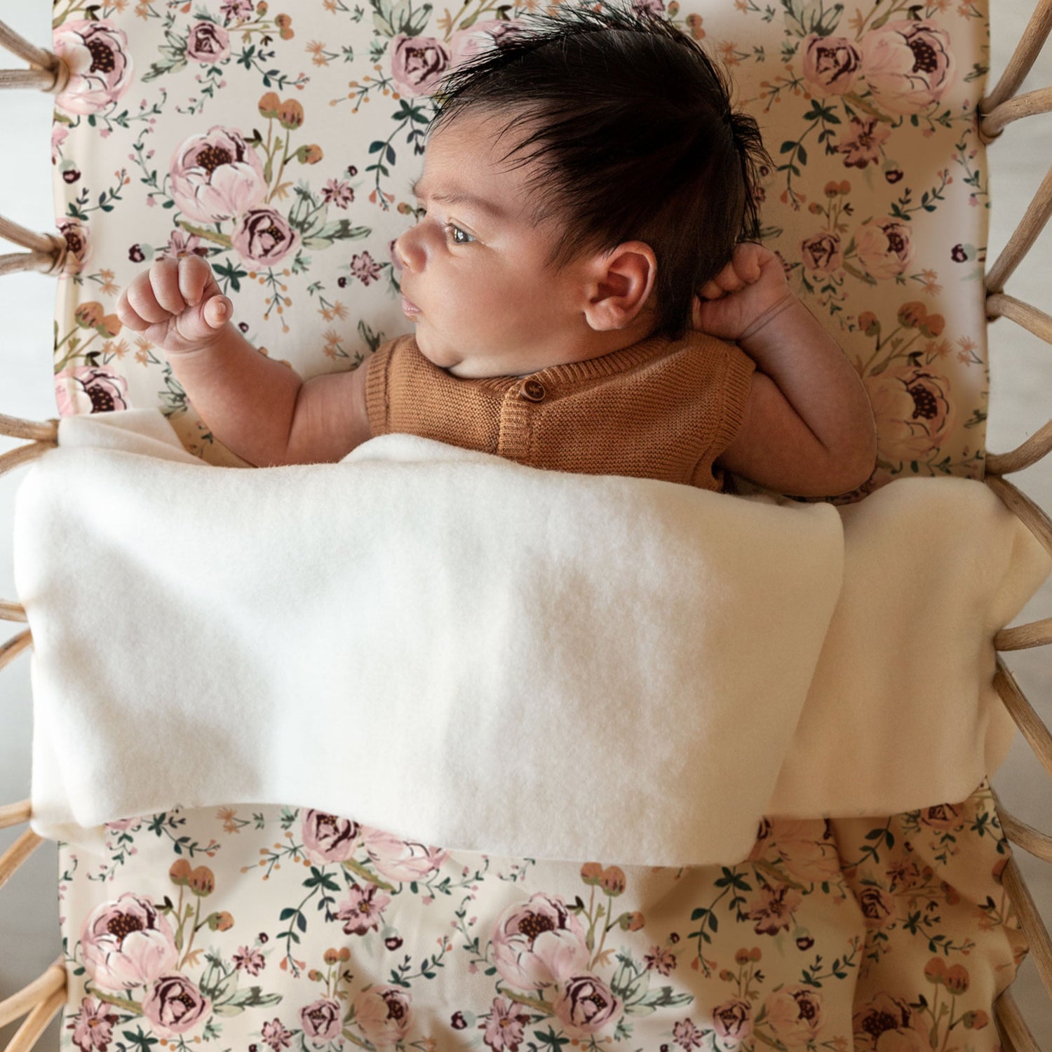 Een vredig kindje rustend in een knus mandje, omringd door een Yumi Baby handgemaakt ontwerp van Ledikantdeken Blamy deken, gekleed in een warme gebreide outfit.