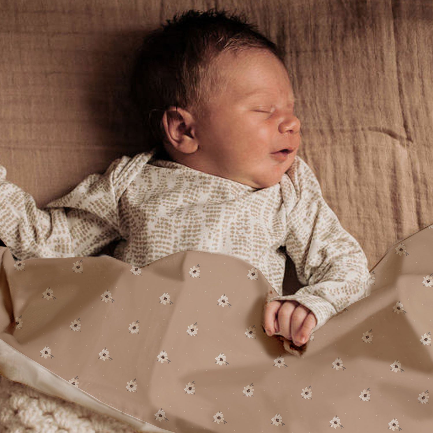 Een vredige pasgeboren baby slaapt in een Yumi Baby Wieglaken Zoe met Dots, knus gewikkeld in een dekentje met delicate patronen.