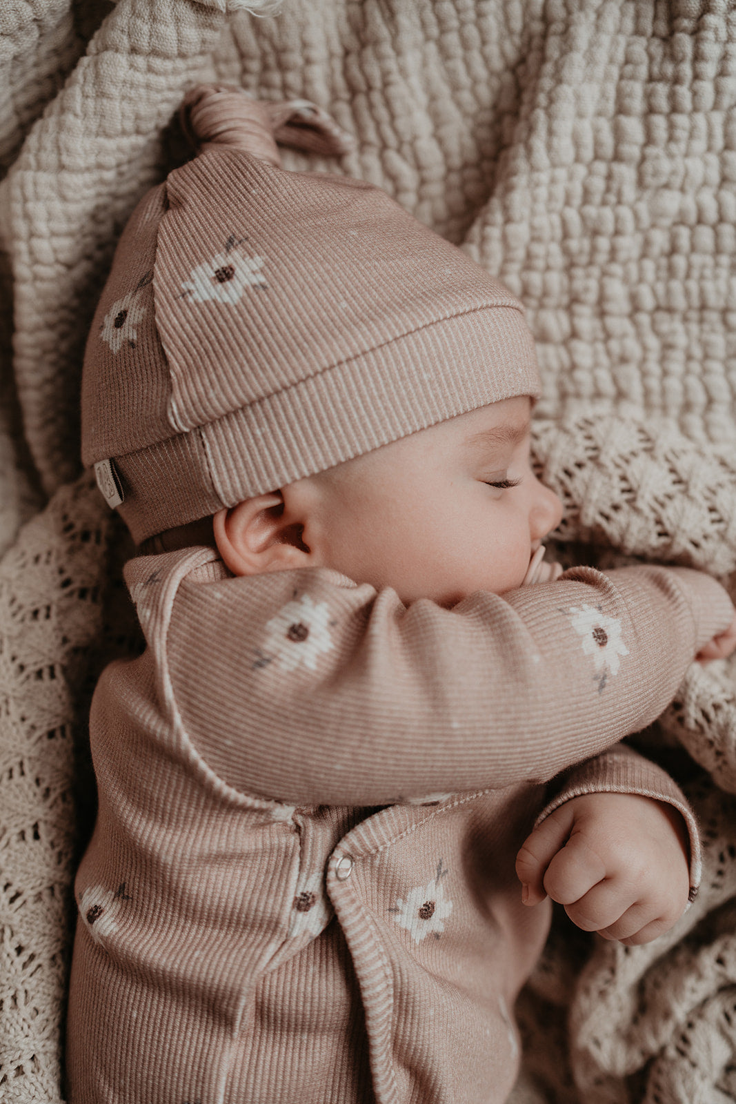 Een vredige slaap: een schattige baby, gezellig gewikkeld in het warme Yumi Baby Overslagshirt Zoë met Dots kleding, dommelt weg in dromenland, genesteld tegen een zachte, gestructureerde deken.