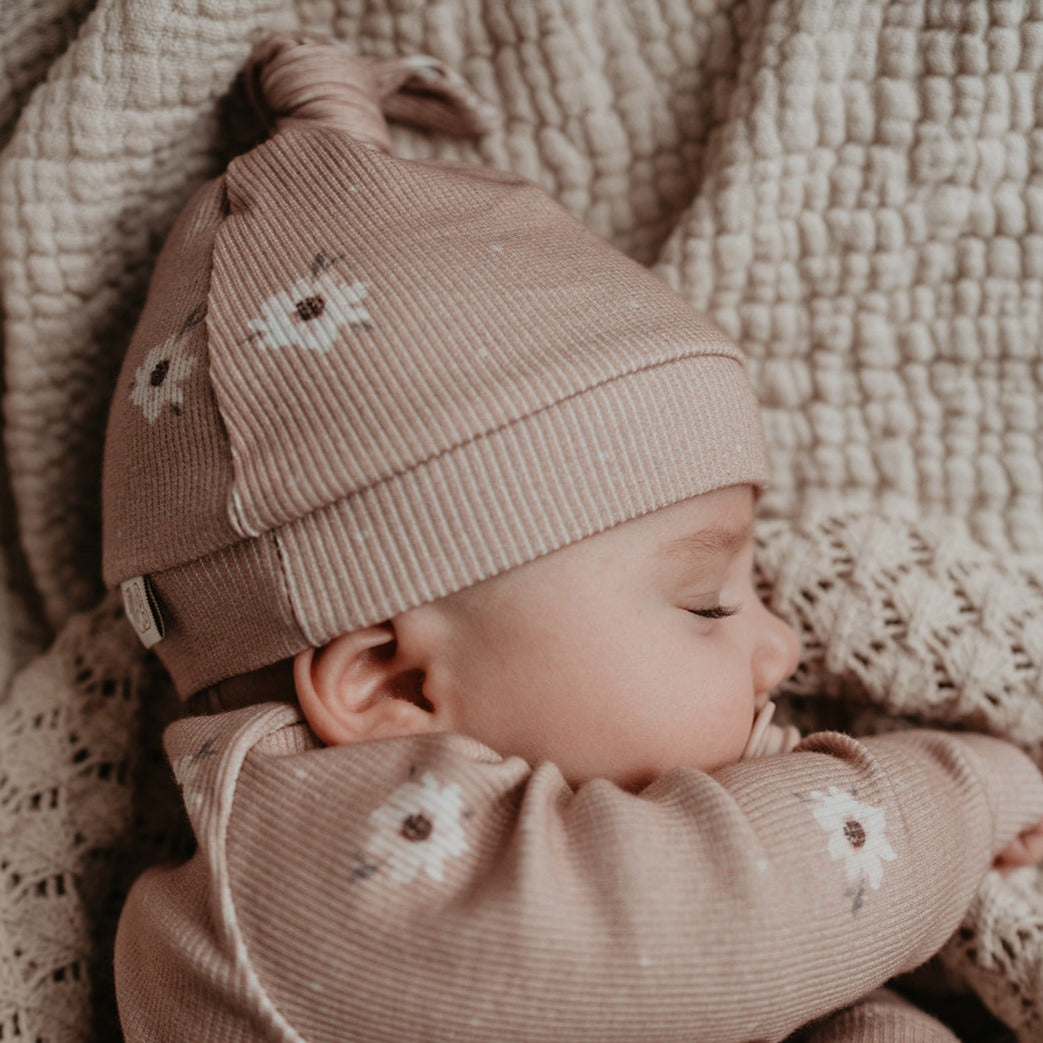 Een pasgeboren baby kleding in een gezellige beige outfit met sterpatronen, liggend op een zachte deken en draagt een kledingstuk Yumi Baby Muts Zoë met Dots.